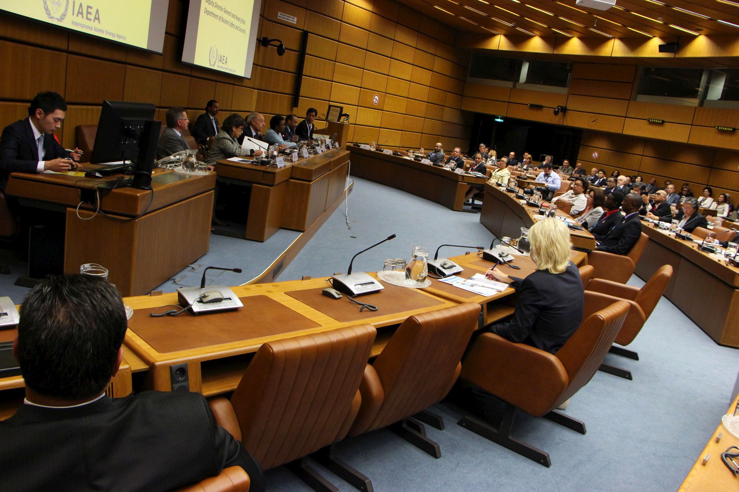 The picture shows the meeting room, which has light brown wooden paneled walls and brown leather chairs. In the picture the meeting is in session.
