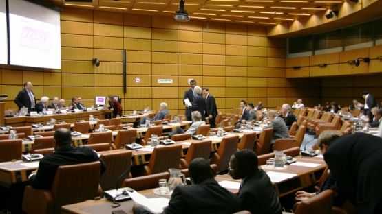 The picture shows the meeting room, which has light brown wooden paneled walls and brown leather chairs. In the picture are meeting attendees in discussion.