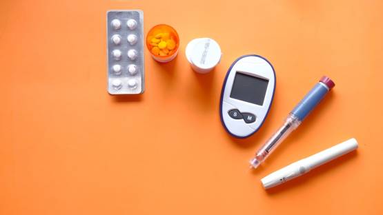 Insulin pen, diabetic measurement tools and pills on orange background.