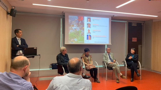 Indoor environment: one scientist leans against a wall and four scientists are seated in front of screen, positioned to speak to an audience. One scientist, Florence Descroix-Comanducci is speaking.